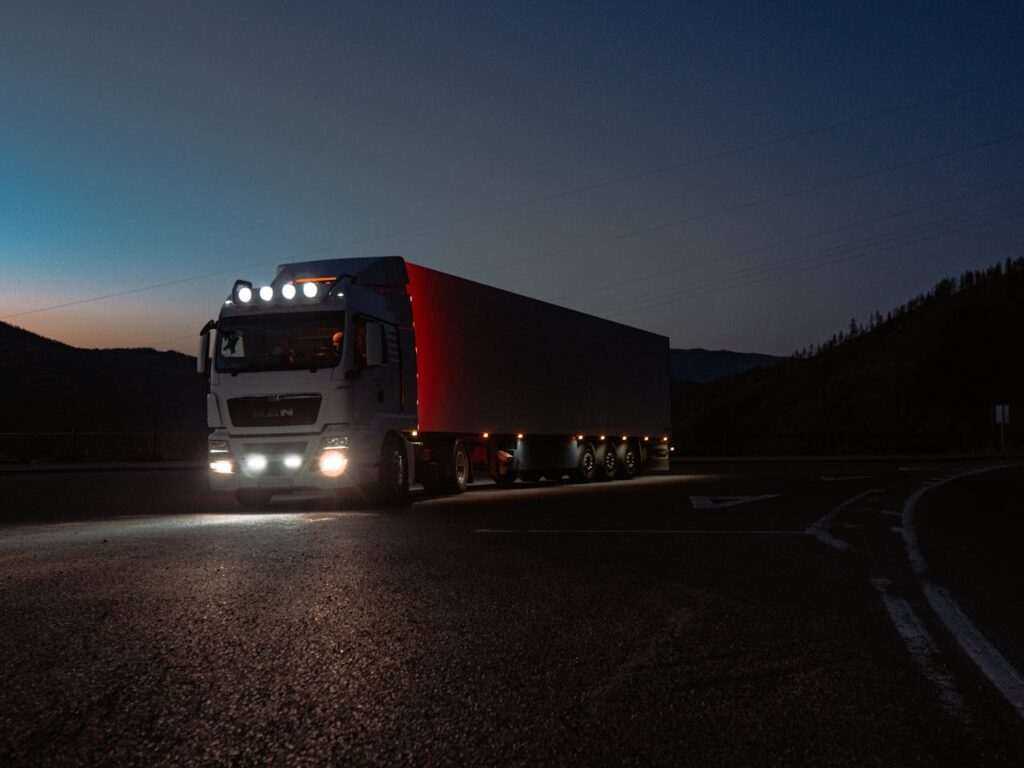pexels-photo-11053641 A heavy-duty truck navigates a quiet road at dusk, highlighting its illuminated path through remote mountains.